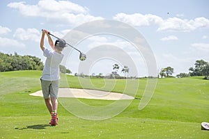 Young man is taking a golf swing in a green field