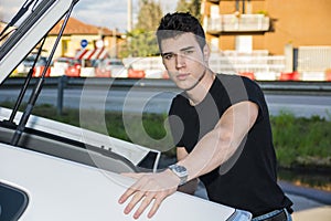 Young man taking luggage and bag out of car trunk