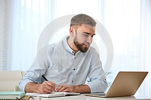 Young man taking notes during online webinar at table