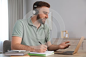 Young man taking notes during online webinar at table