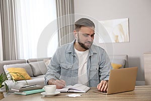 Young man taking notes during online webinar at table indoors