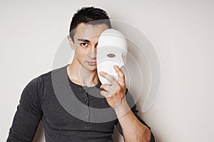 Young man taking off white mask revealing face and identity