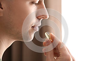 Young man taking pill indoors, closeup