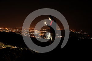 Young man taking selfie on top of the hill observing the night city view.