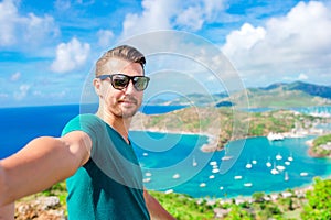 Young man taking selfie with view of English Harbor from Shirley Heights, Antigua, paradise bay at tropical island in