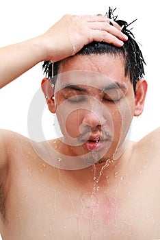 Young man taking a shower and standing under flowing water in bathroom