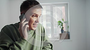 The young man is talking briskly on the phone. In the background, a girl wanders the room