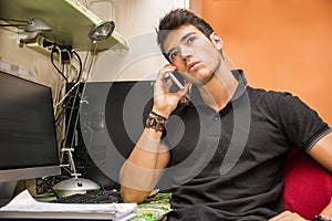 Young Man Talking on Cell Phone at Computer Desk