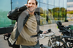 Young man talking on cellphone while standing with bicycle outside