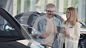 Young man talking female seller while choosing car at salon