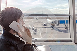 Young man talking by mobile phone in airport hall while hi is waiting for boarding plane.