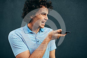 Young man talking on mobile phone with his girlfriend. Happy male with curly hair resting outside making a call on his smart phone