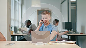 Young man talking mobile phone at office. Smiling guy speaking on cellphone