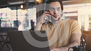 Young man talking mobile phone and using laptop computer in cafe