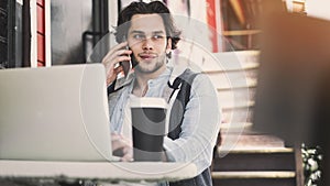 Young man talking mobile phone and using laptop computer in cafe