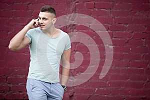 Young man talking on the phone in front of brick wall