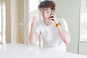 Young man talking on the phone at home annoyed and frustrated shouting with anger, crazy and yelling with raised hand, anger