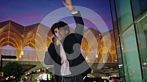 Young man talking phone at illuminated city. Smiling businessman waving arm