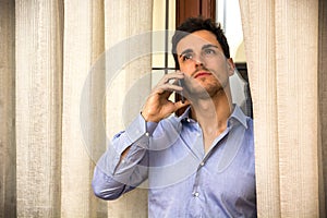 Young man talking on the phone next to curtains