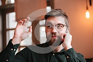 Young man talking by phone and waving look aside.