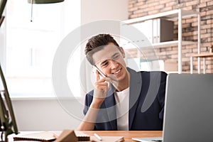 Young man talking on phone while working with laptop indoors