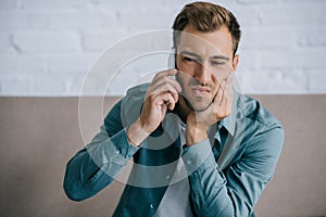 young man talking by smartphone and suffering from jaw pain photo