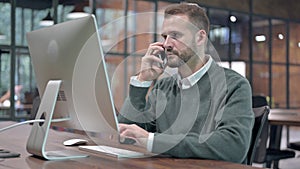 Young Man talking Smartphone while using Desktop