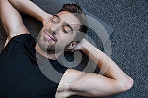 Young man in tanktop lying on a yoga mat with eyes closed and hands