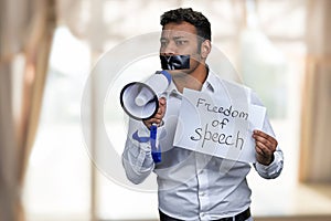 Young man with taped mouth trying to speak into megaphone.