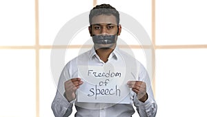 Young man with taped mouth on windows background.