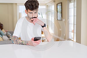 Young man with tattoo wearing casual white t-shirt using smartphone