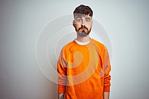 Young man with tattoo wearing orange sweater standing over isolated white background puffing cheeks with funny face