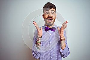 Young man with tattoo wearing purple shirt and bow tie over isolated white background celebrating crazy and amazed for success