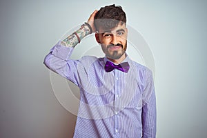 Young man with tattoo wearing purple shirt and bow tie over isolated white background confuse and wonder about question