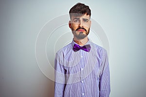 Young man with tattoo wearing purple shirt and bow tie over isolated white background depressed and worry for distress, crying