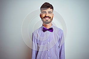 Young man with tattoo wearing purple shirt and bow tie over isolated white background with a happy and cool smile on face