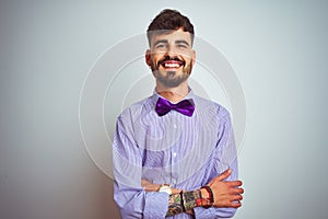Young man with tattoo wearing purple shirt and bow tie over isolated white background happy face smiling with crossed arms looking