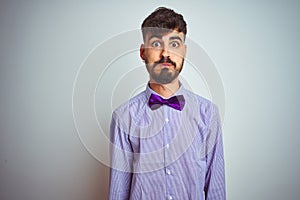 Young man with tattoo wearing purple shirt and bow tie over isolated white background puffing cheeks with funny face