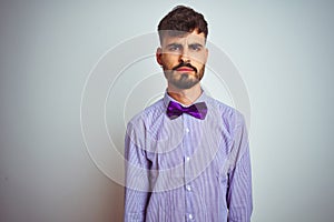 Young man with tattoo wearing purple shirt and bow tie over isolated white background skeptic and nervous, frowning upset because