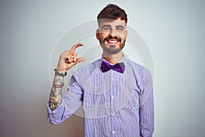 Young man with tattoo wearing purple shirt and bow tie over isolated white background smiling and confident gesturing with hand