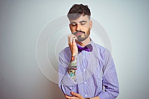 Young man with tattoo wearing purple shirt and bow tie over isolated white background thinking looking tired and bored with