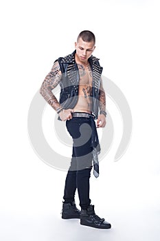 A young man with tattoos in a black leather vest with rhinestones and black jeans