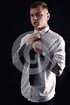 Young man with tattoos wearing shirt and tie on black background