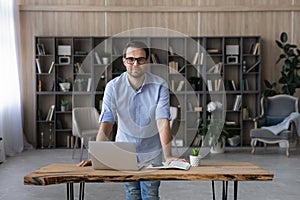 Young man teacher stand in classroom lean on work desk