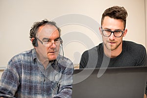 Young man teaching eldery man of usage of computer. Intergenerat