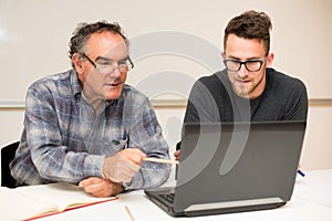 Young man teaching eldery man of usage of computer. Intergenerational transfer of computer skills.