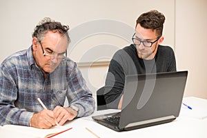 Young man teaching eldery man of usage of computer. Intergenerational transfer of computer skills.