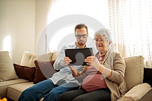 Young man teaching his grandmother how to use a tablet