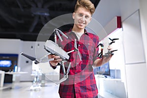 Young man is in the technology store with drones in his hands.man holds a quadcopter in his arms and smiles