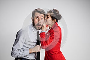 Young man telling gossips to his woman colleague at the office